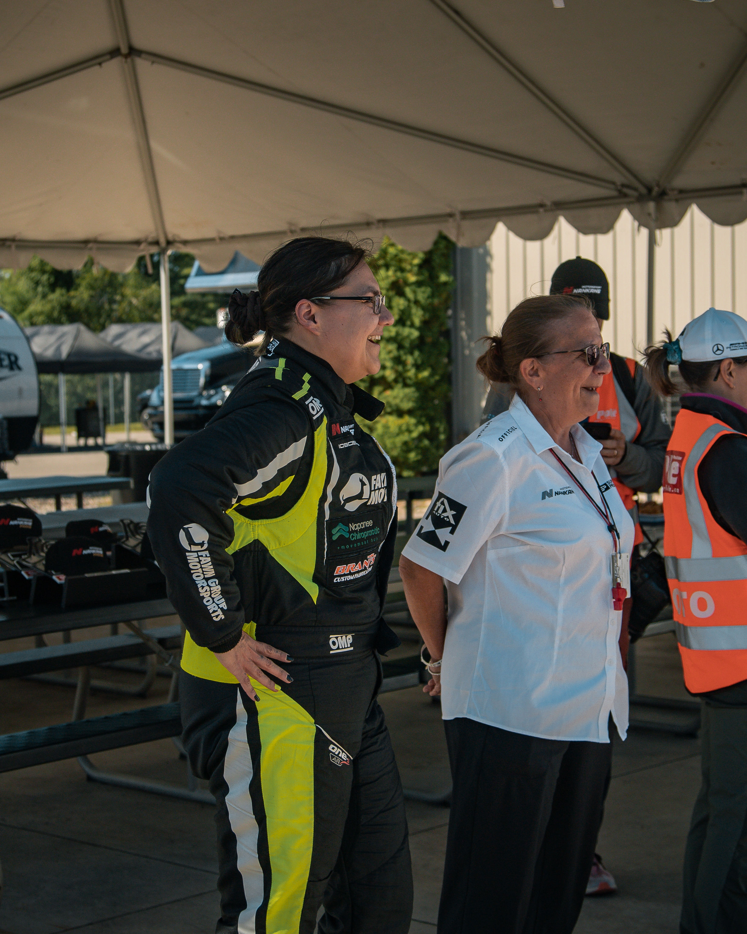 Tamara smiling with race official under paddock tent in Fawn Group suit